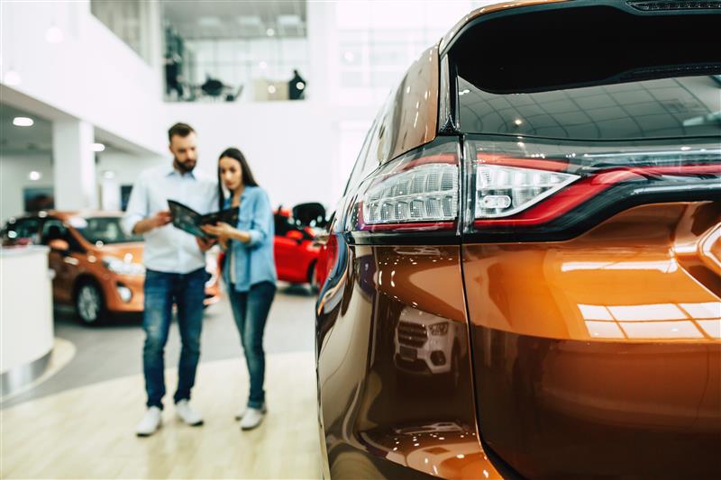 Couple standing in a car dealership reviewing a brochure while shopping for a new vehicle.