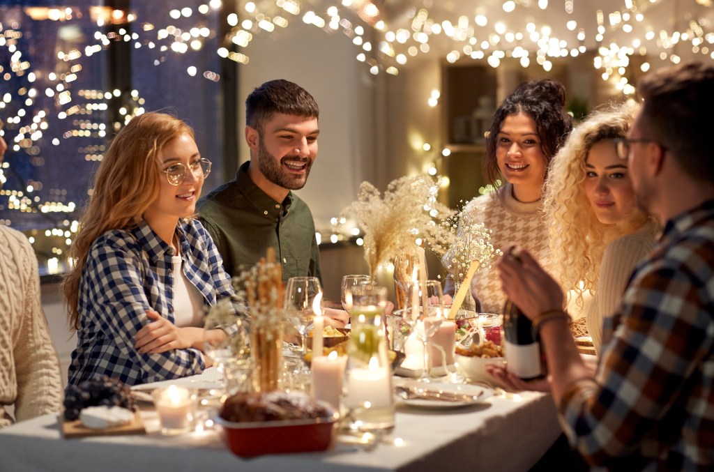 Friends at a simple holiday table with string lights, snacks and non-alcoholic punch in a cozy living room.