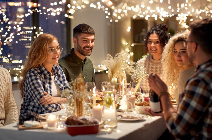 Friends at a simple holiday table with string lights, snacks and non-alcoholic punch in a cozy living room.